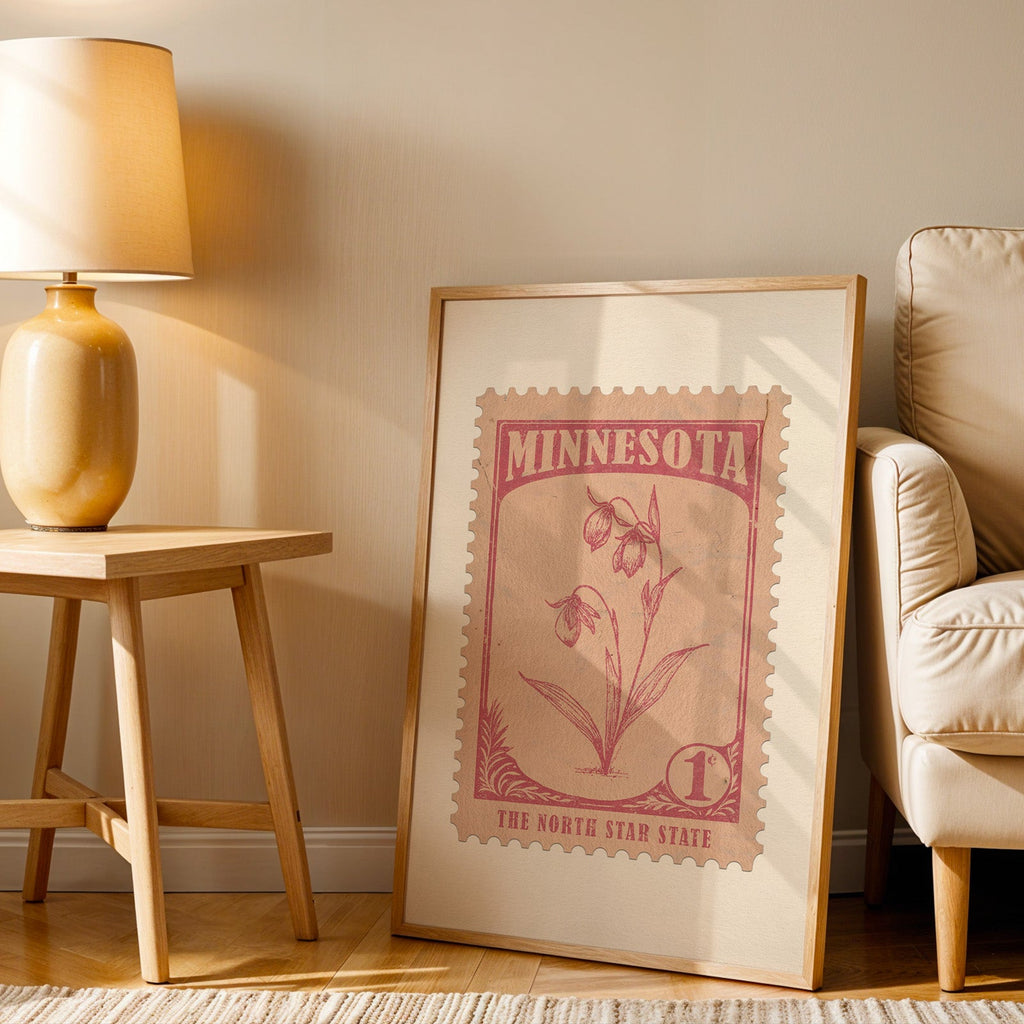 Minnesota stamp print in a wood frame resting on the floor beside a beige armchair and a yellow lamp