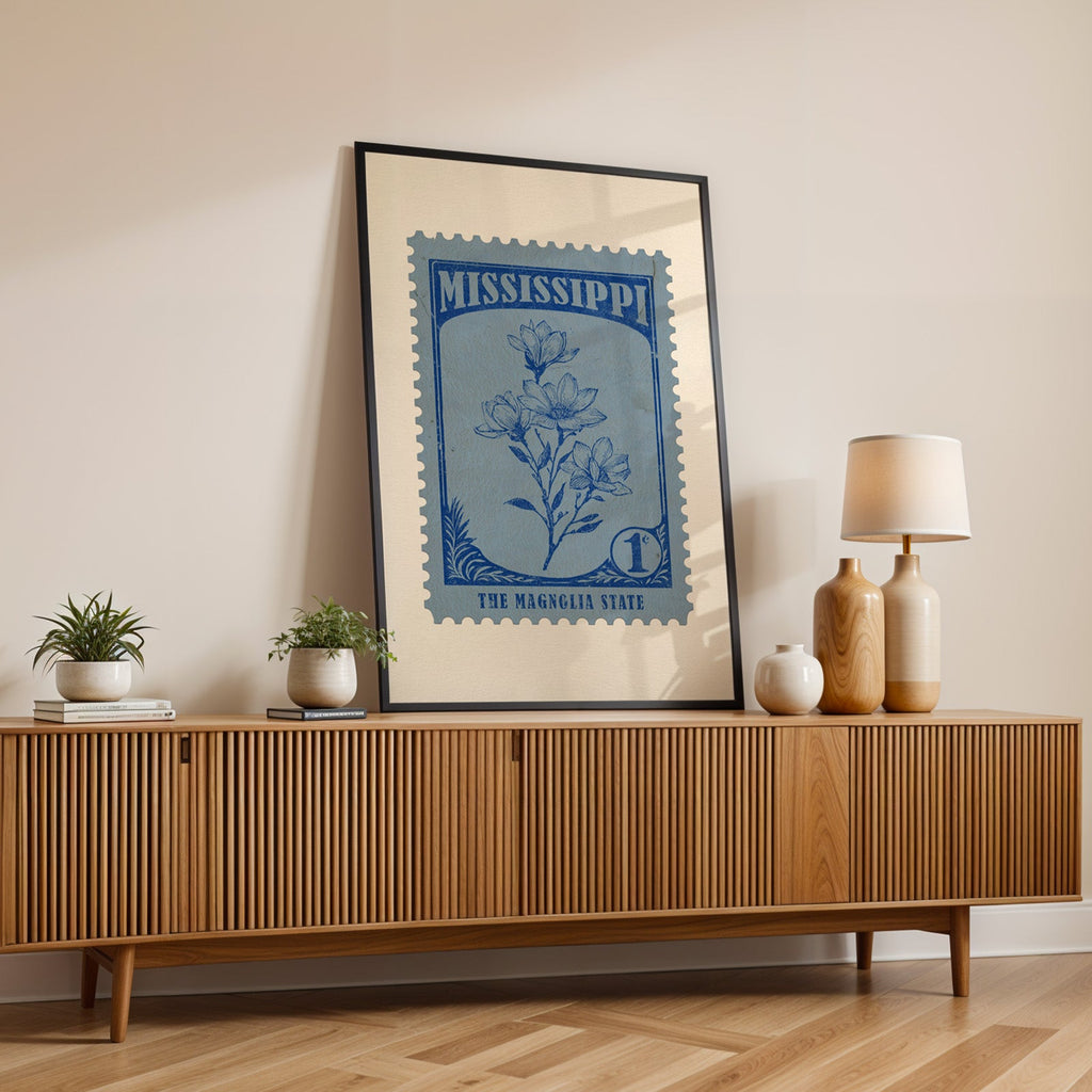 Mississippi state flower print in a black frame leaning on a fluted wood credenza with vases and a lamp
