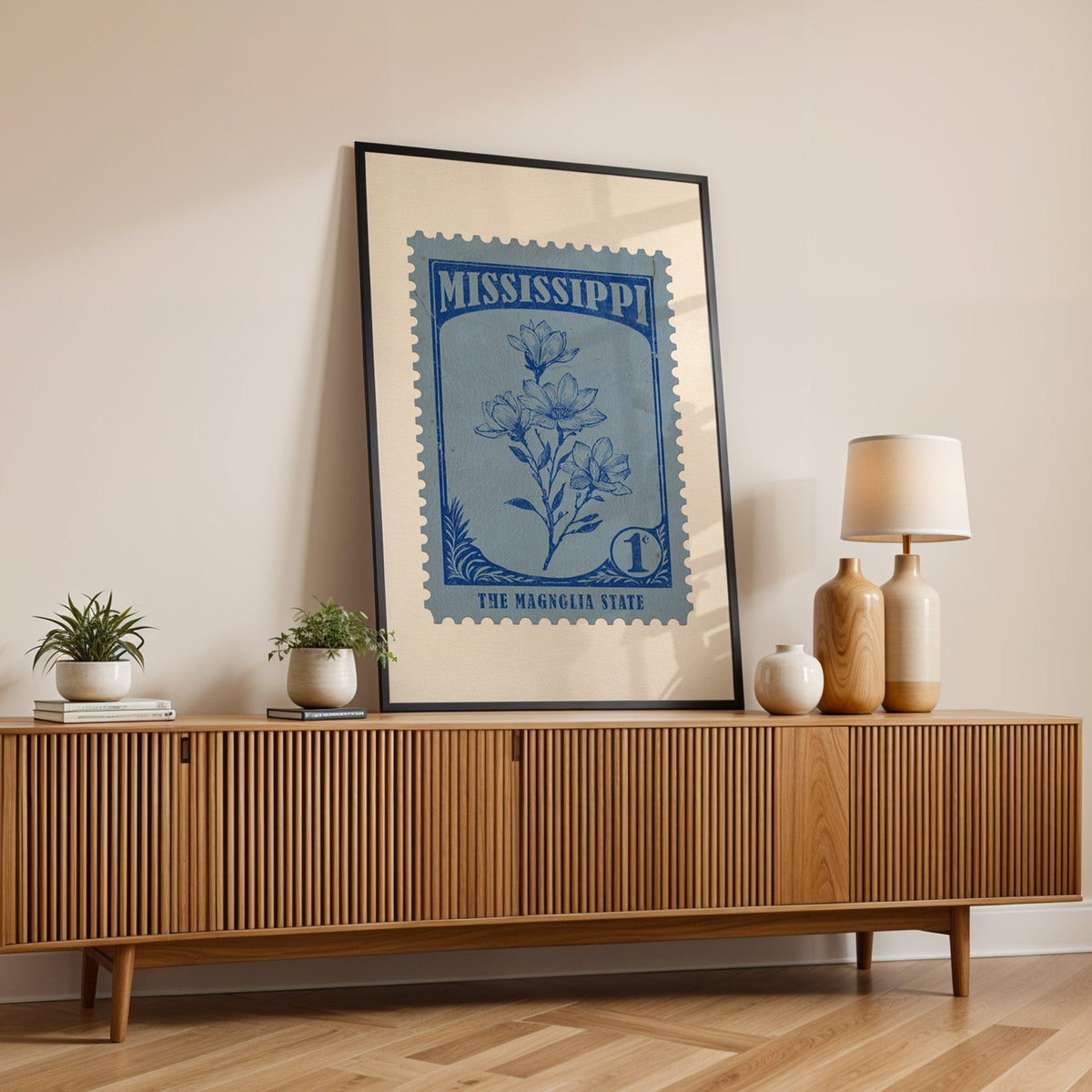 Mississippi state flower print in a black frame leaning on a fluted wood credenza with vases and a lamp