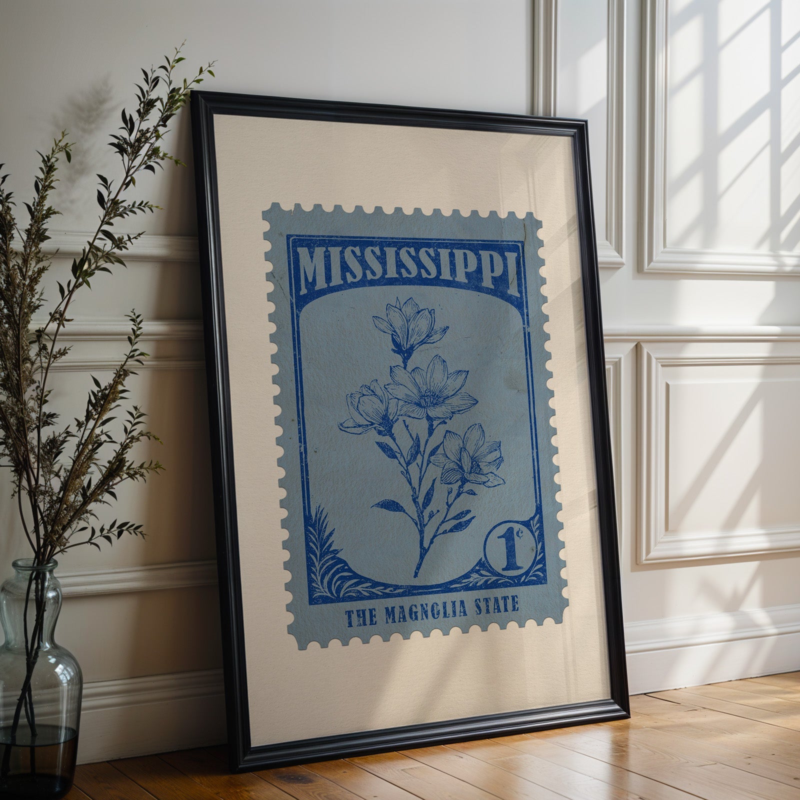 Mississippi state flower print in a black frame leaning against a white panelled wall beside olive branches