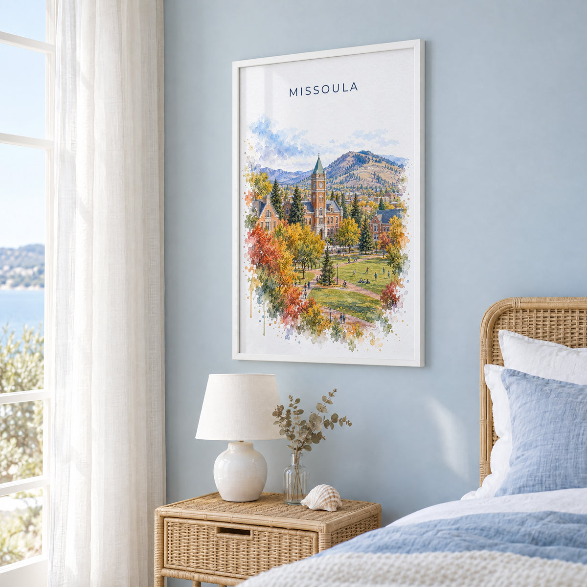 Missoula watercolor print in a white frame on a pale blue wall beside a rattan bed in a coastal bedroom
