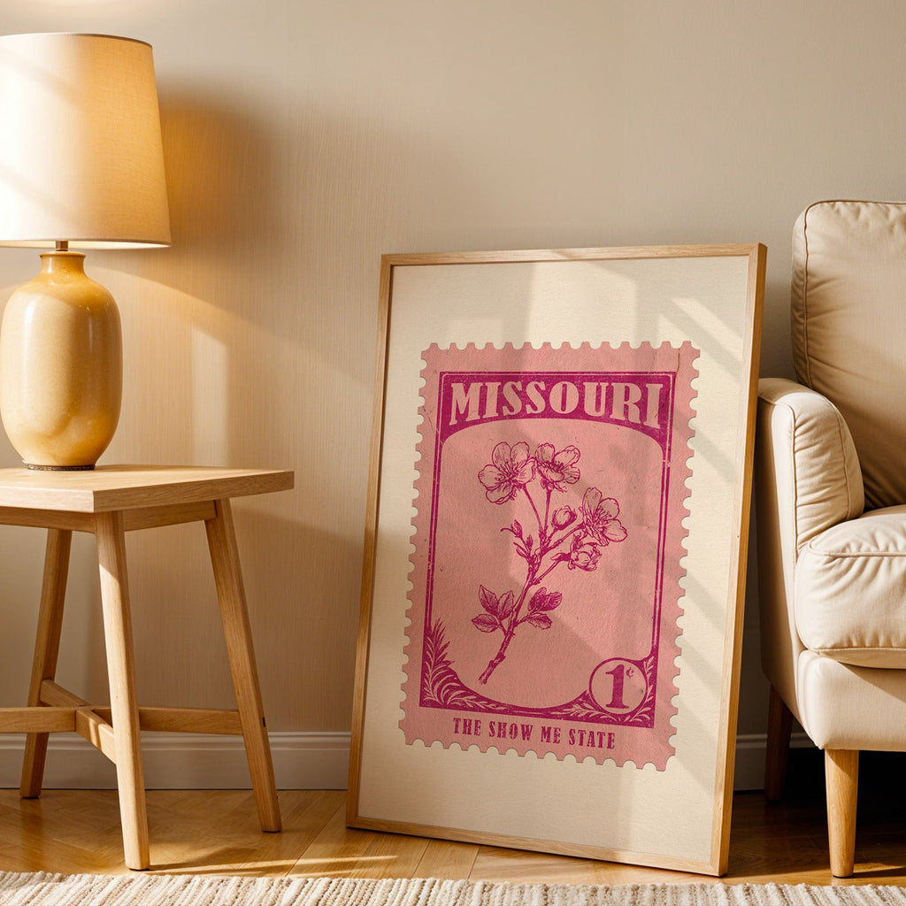 Missouri stamp print in a wood frame resting on the floor beside a beige armchair and a yellow lamp
