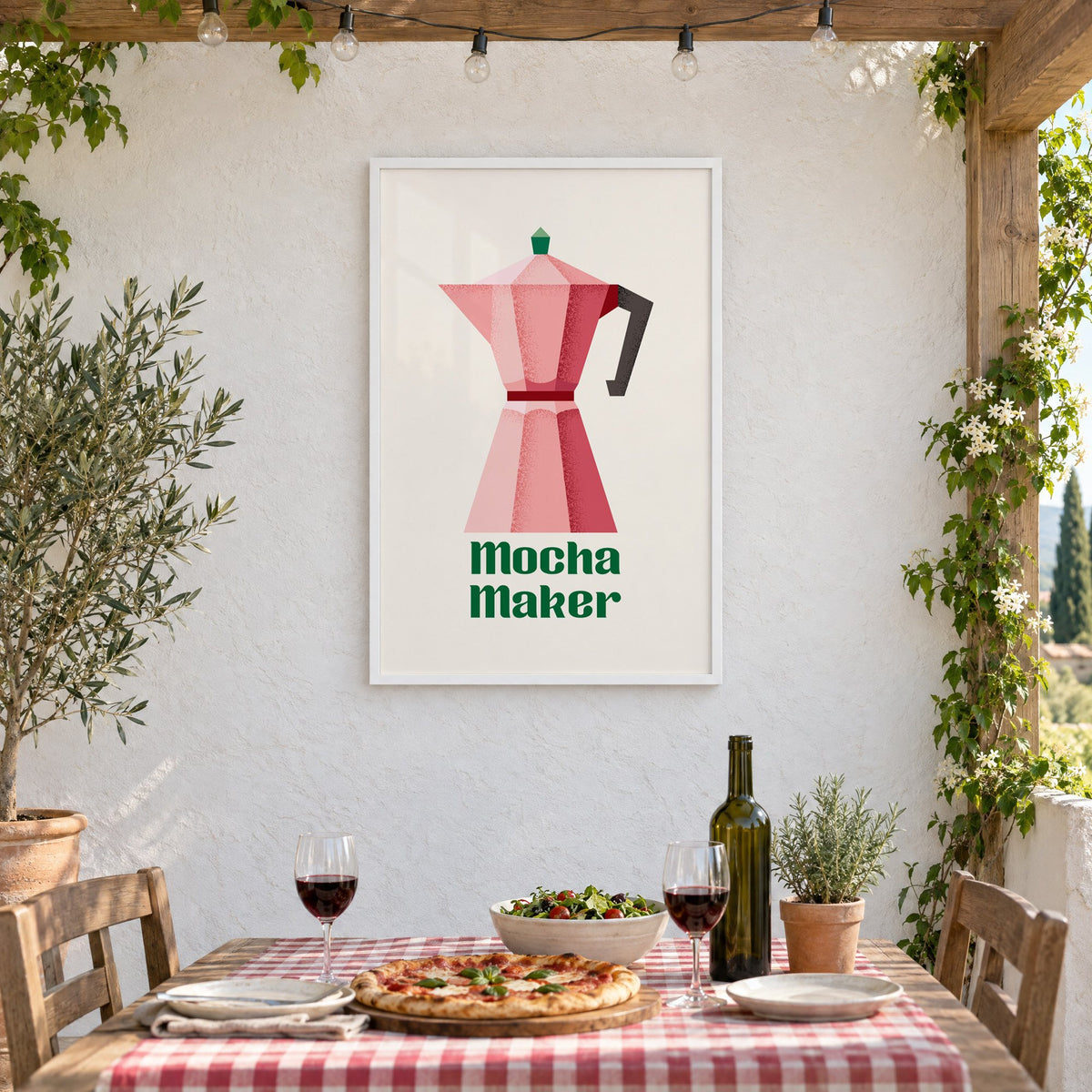 Mocha Maker pink moka pot print in a white frame on a stucco wall above a checked-cloth table with pizza and red wine