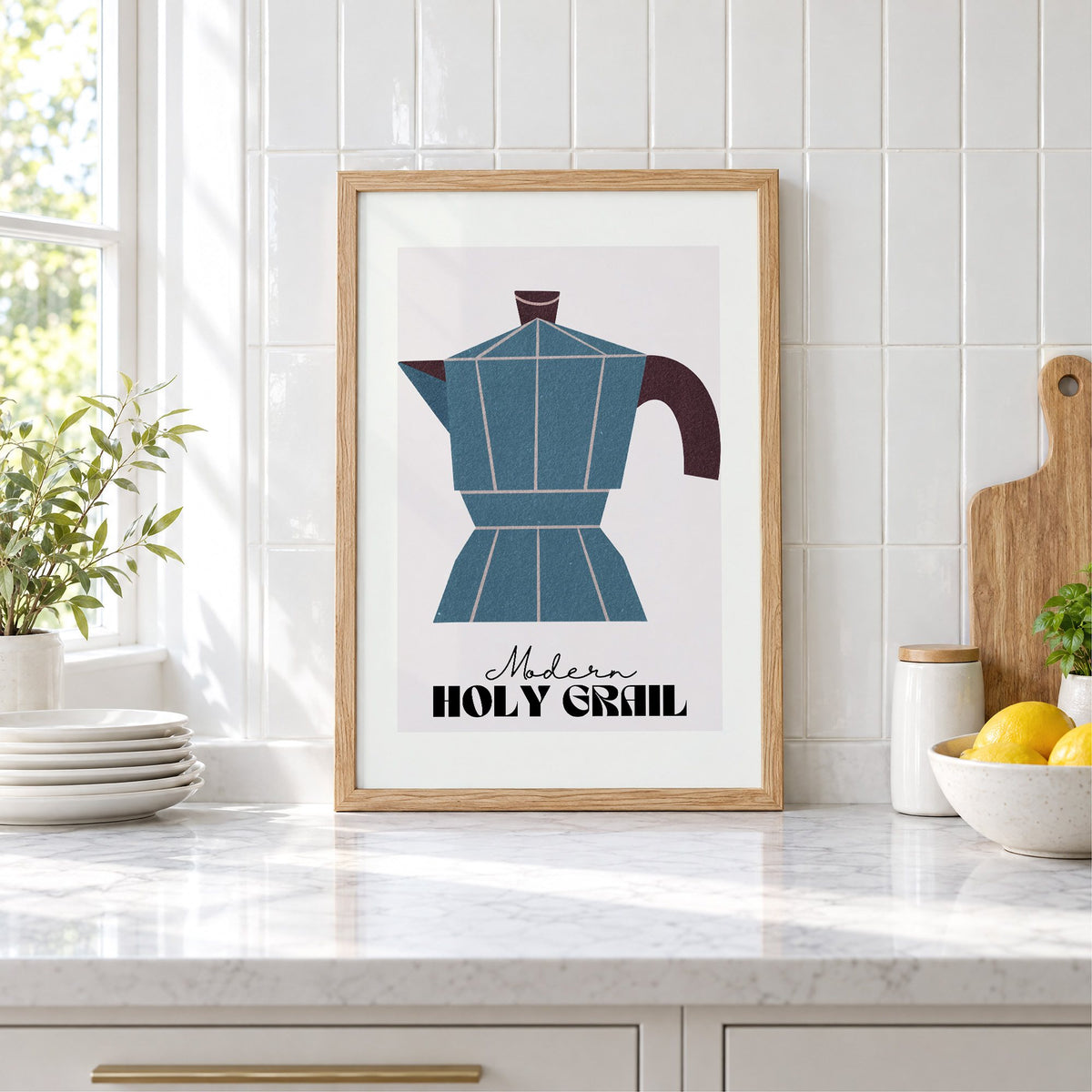 Modern Holy Grail moka pot print in an oak frame leaning on a marble counter by white tiles and lemons