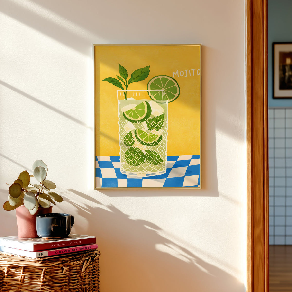 Mojito print in a gold frame above a basket of books and a pilea plant