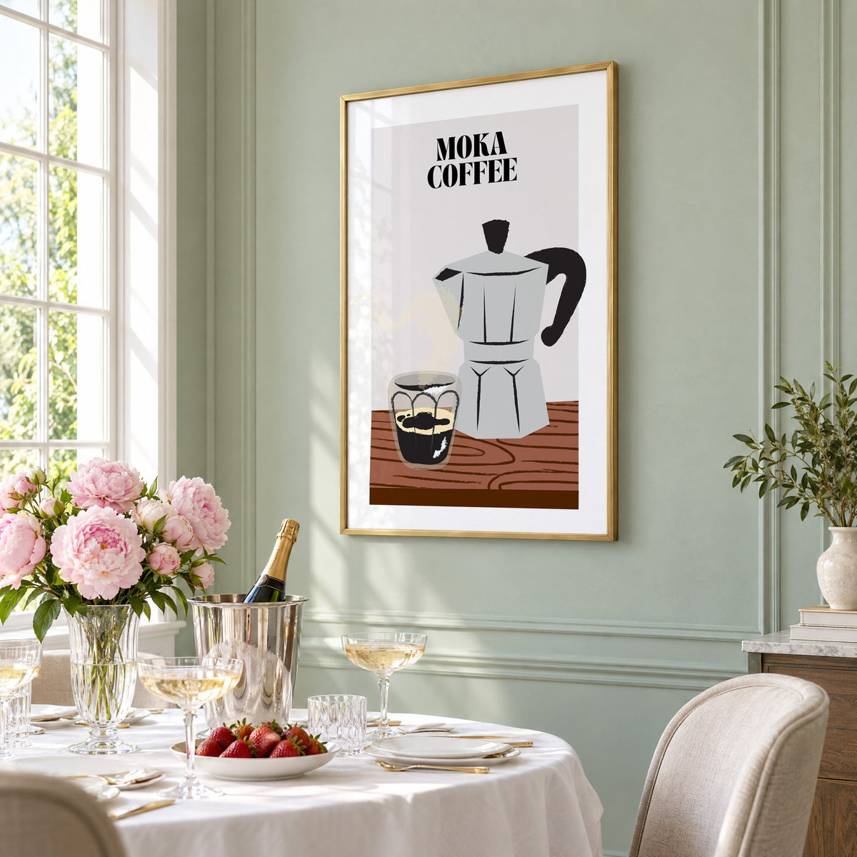 MOKA COFFEE silver pot wood table print in a brass frame on a sage wall above a brunch table with champagne and peonies, seen at an angle