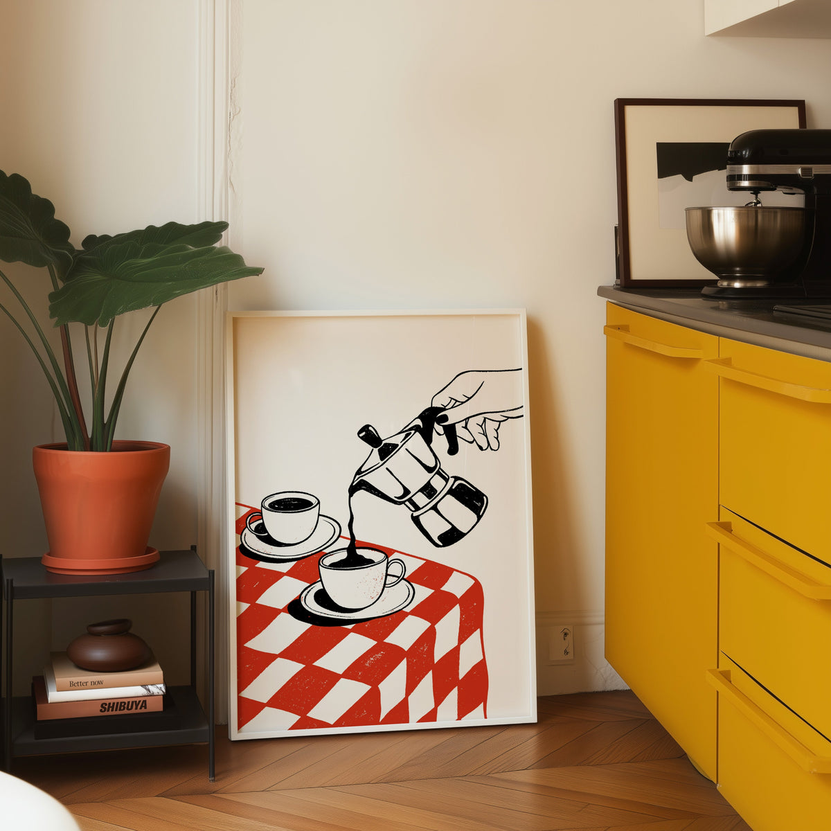 Moka pot print in a white frame leaning on parquet beside a bright yellow kitchen