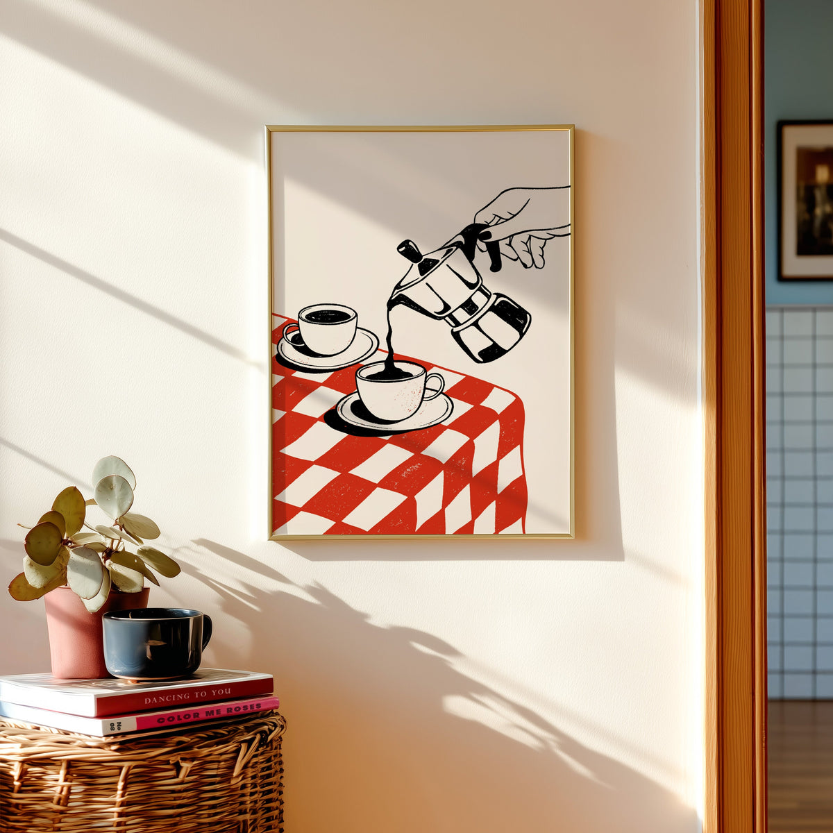 Moka pot print in a gold frame above a basket of books and a pilea plant