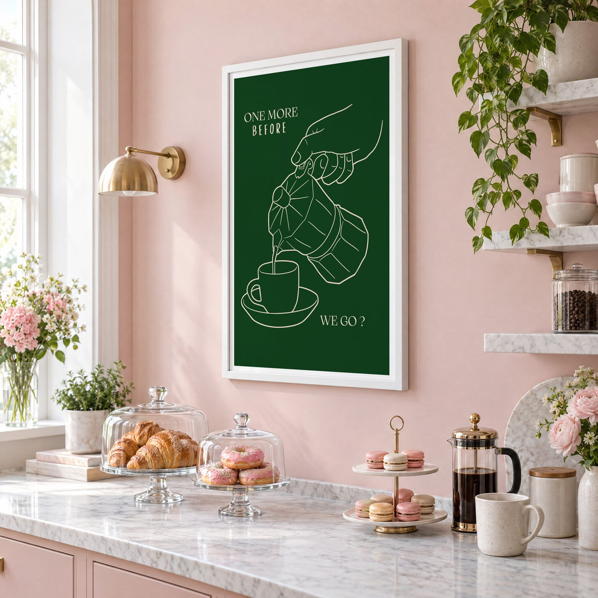 ONE MORE BEFORE WE GO? moka pot line print in a white frame on a blush pink wall above a patisserie counter with croissants and macarons, seen at an angle