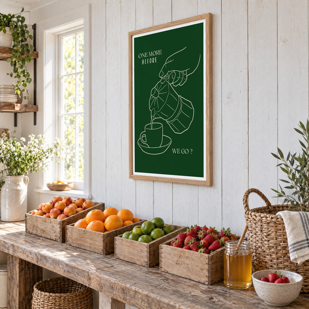 ONE MORE BEFORE WE GO? moka pot line print in an oak frame on white plank walls above wooden crates of fresh fruit, seen at an angle