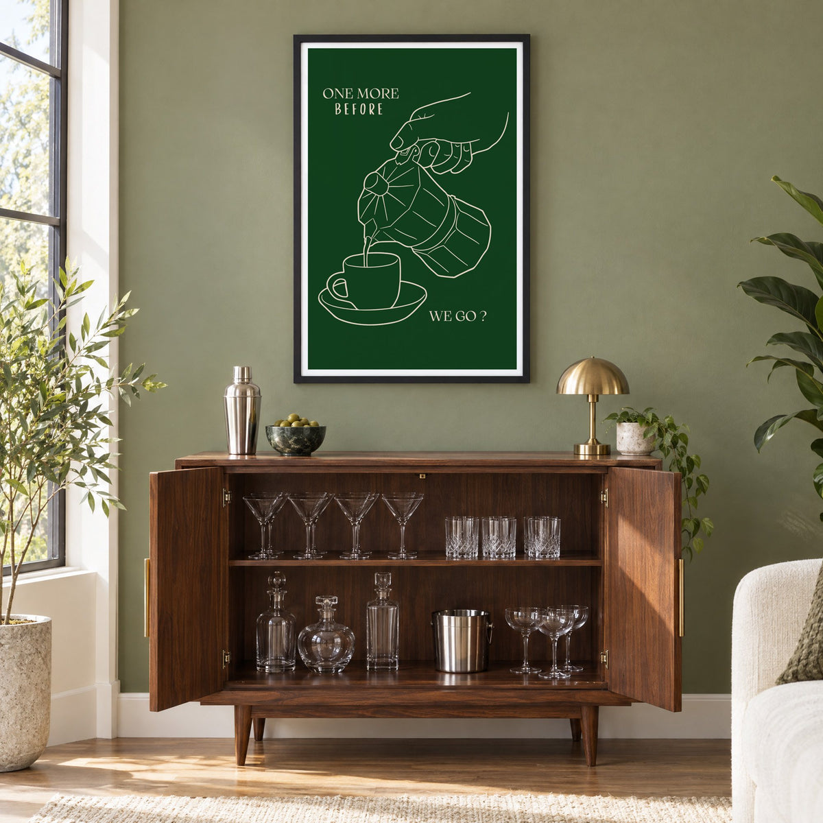 ONE MORE BEFORE WE GO? moka pot line print in a black frame on an olive green wall above a walnut bar cabinet with glassware