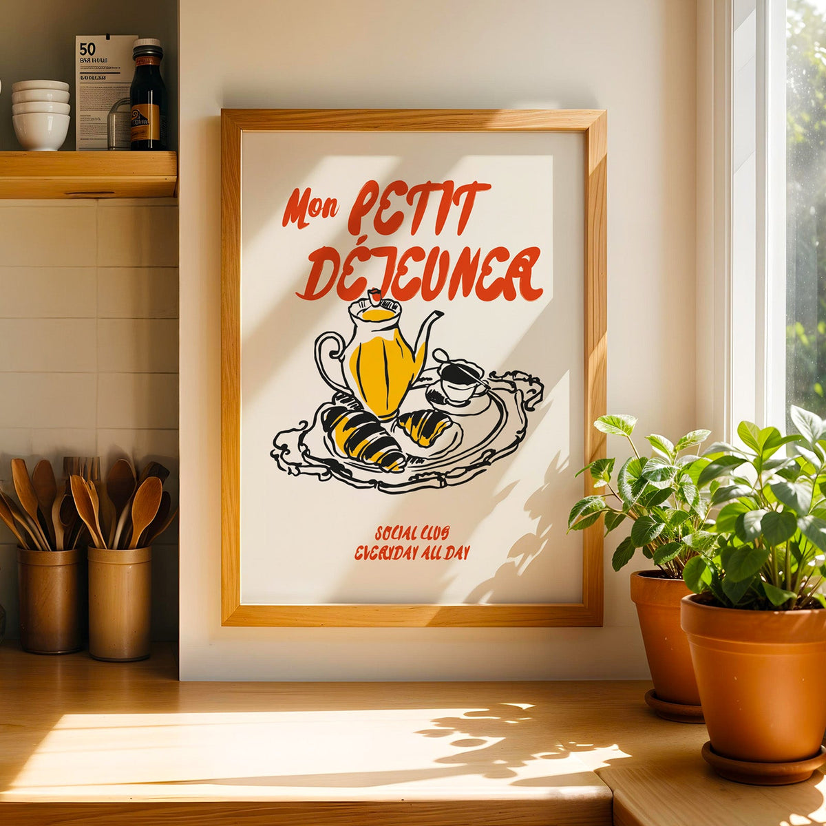 Mon Petit Dejeuner croissants print in a light pine frame beside a jar of wooden spoons