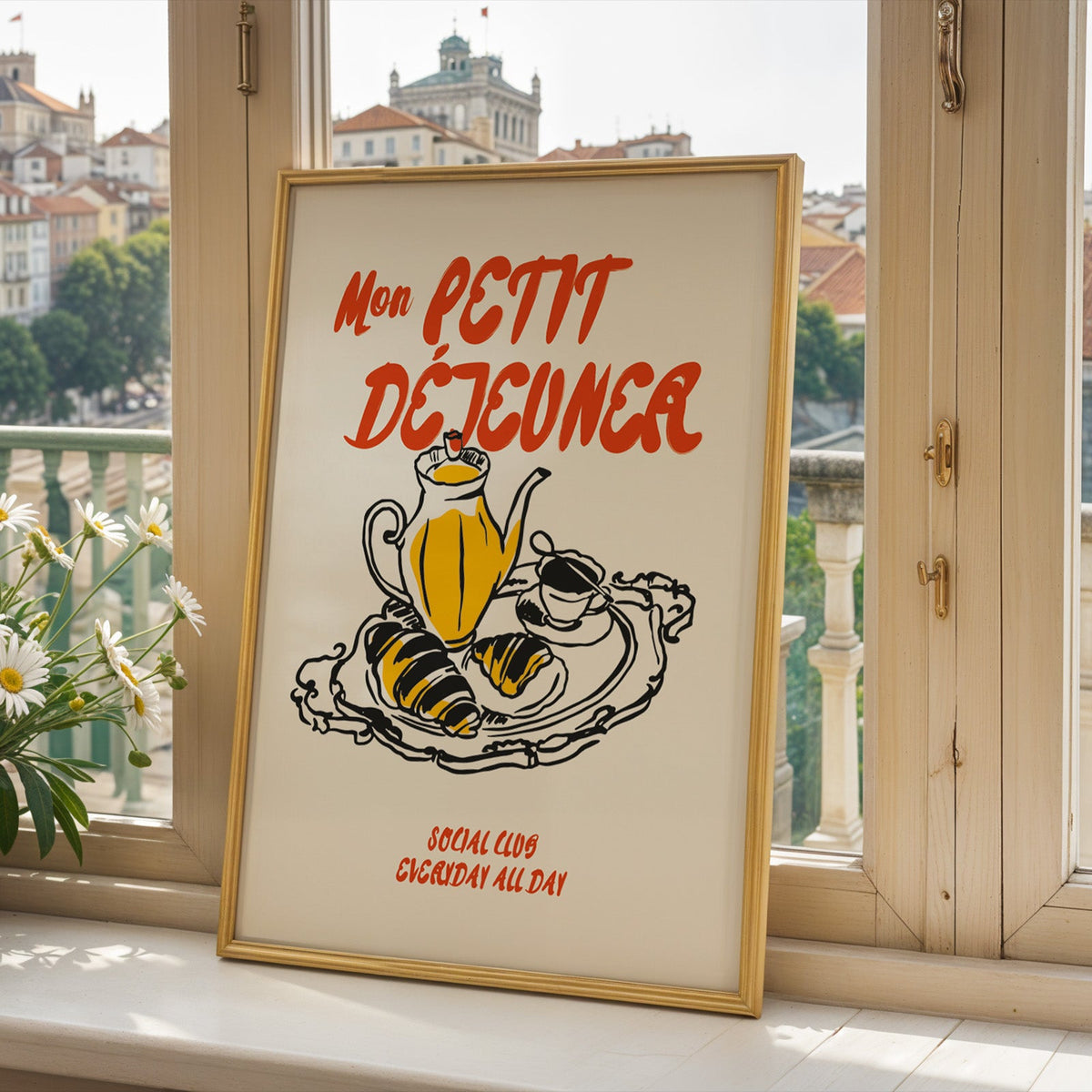 Mon Petit Dejeuner croissants print in a gold frame on a window sill above a town