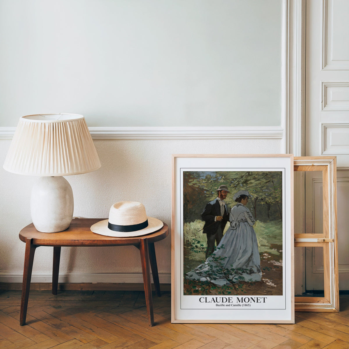 Monet forest print in a light wood frame leaning by a bench and panama hat