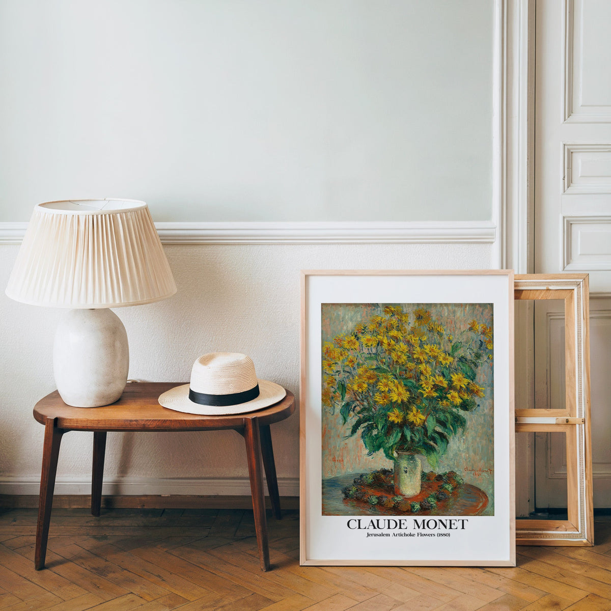 Monet floral poster in a light wood frame leaning by a bench and panama hat