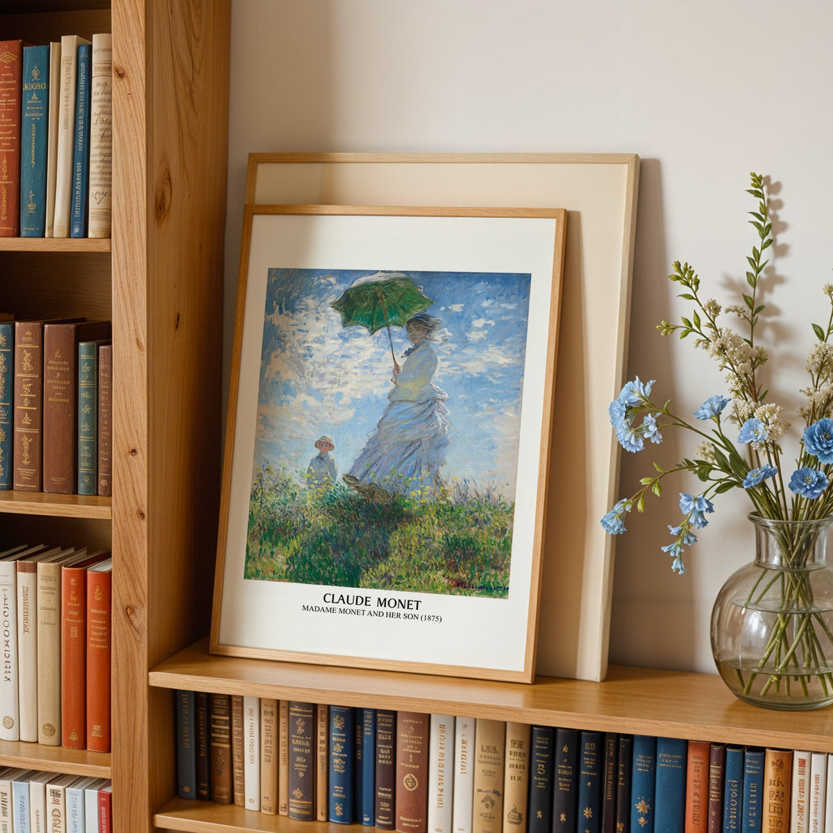 Monet print in an oak frame leaning on a bookshelf beside blue flowers