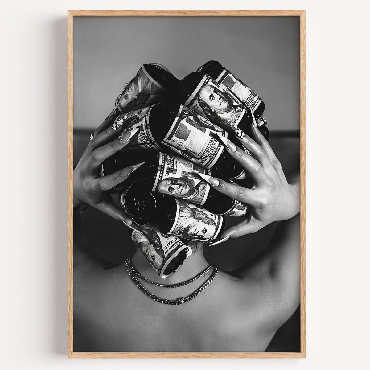 Hair curlers wrapped in dollar bills from behind print in a light oak frame on a plain white wall
