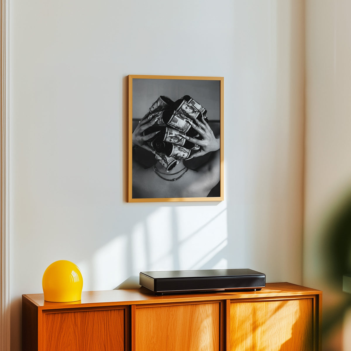Hair curlers wrapped in dollar bills from behind print in an oak frame above a teak sideboard with a yellow glass lamp