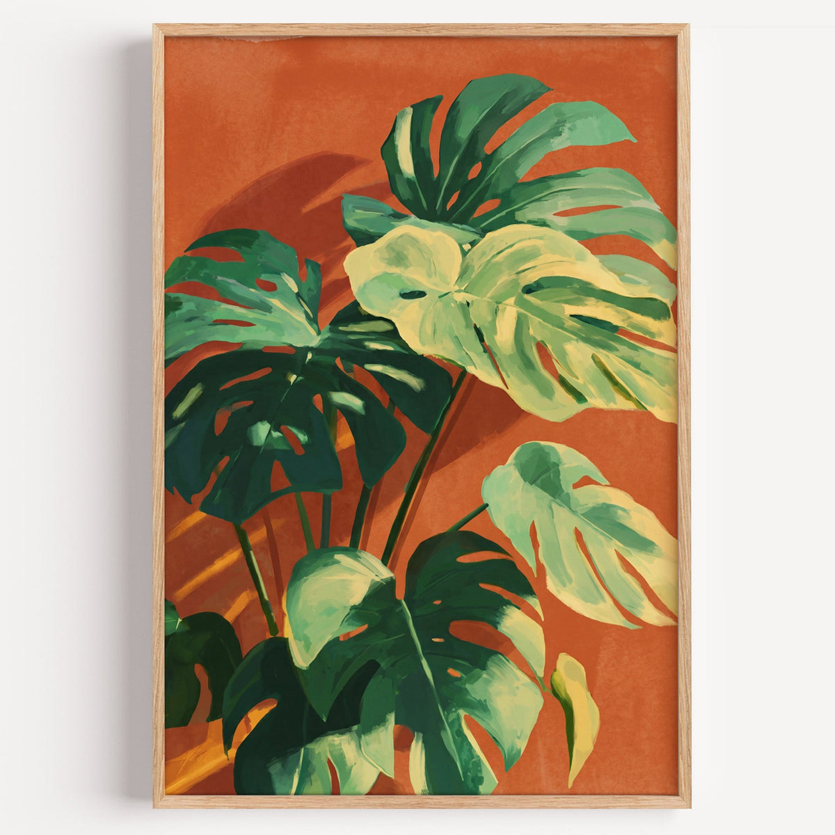 Monstera leaves on terracotta print in a light oak frame on a plain white wall