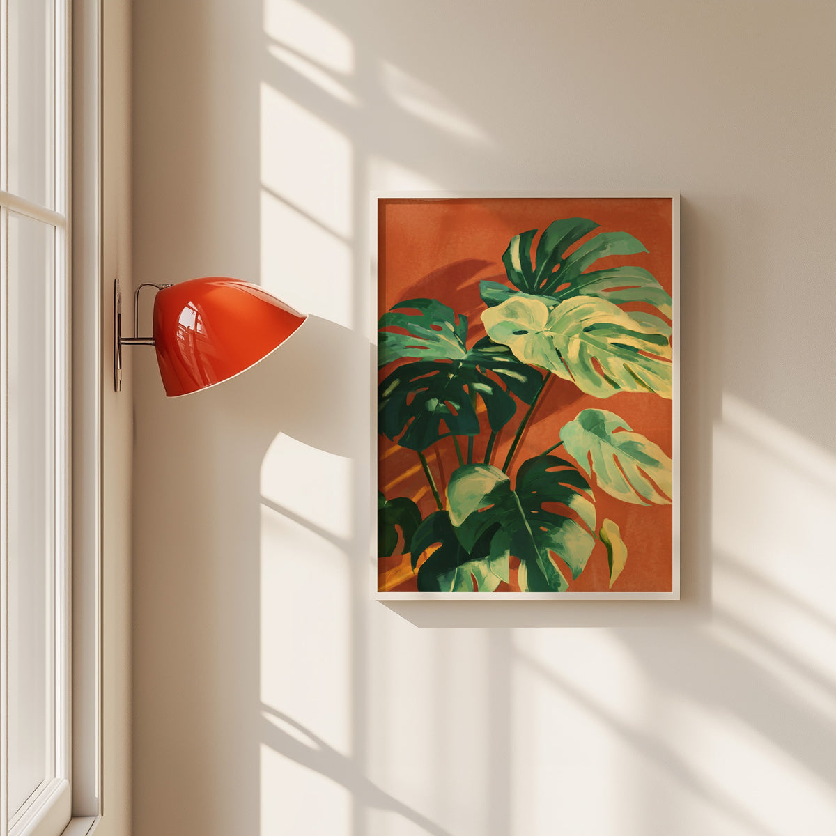 Monstera leaves on terracotta print in a white frame beside a red wall sconce
