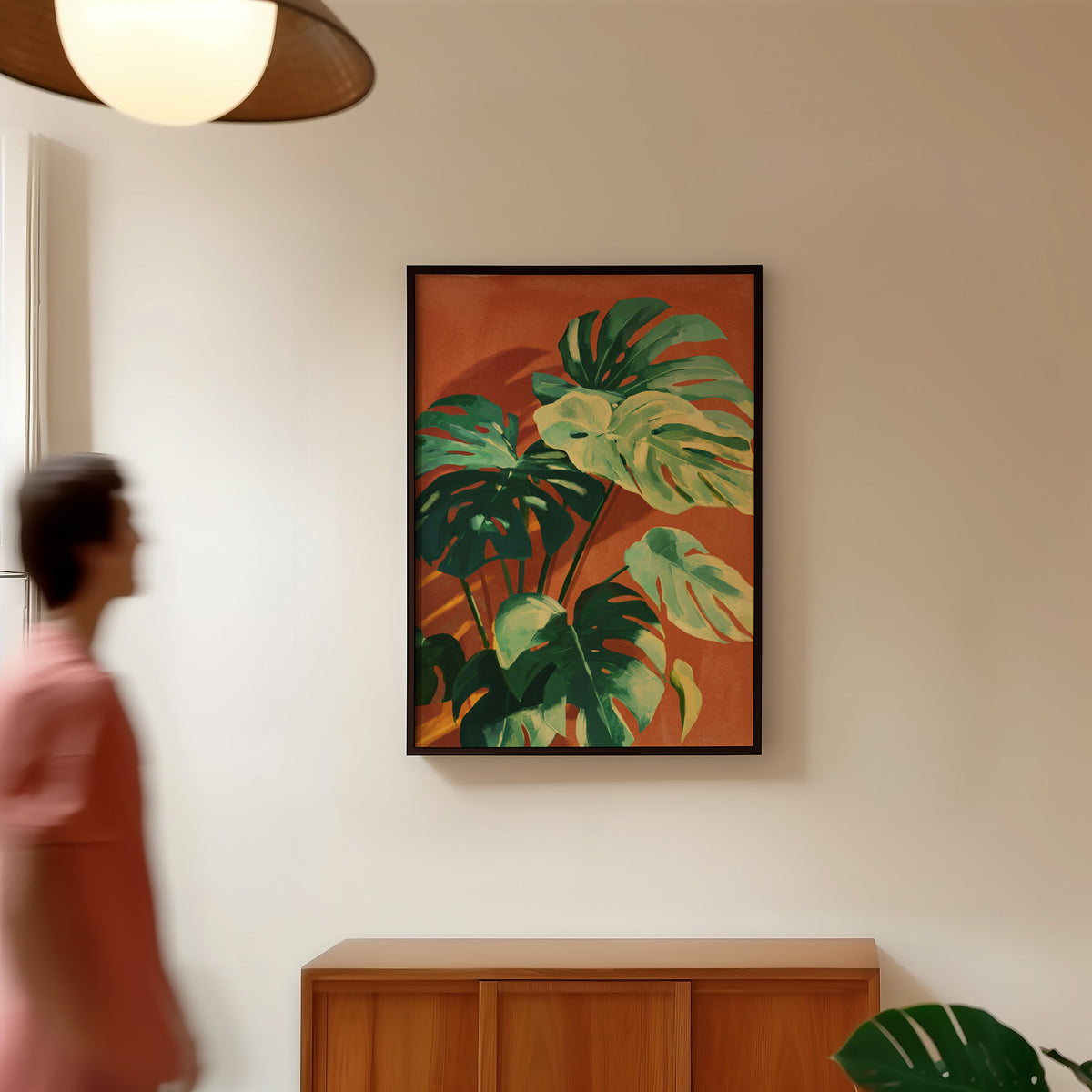 Terracotta and green leaf print in a black frame in a hallway under a rattan pendant