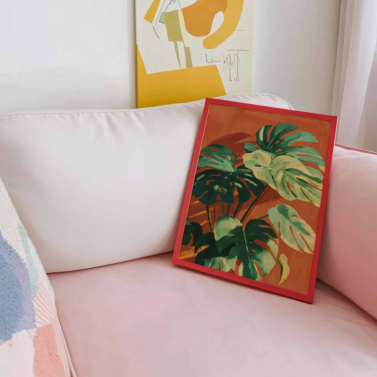 Sunlit monstera print shown in a red frame leaning on a blush pink sofa