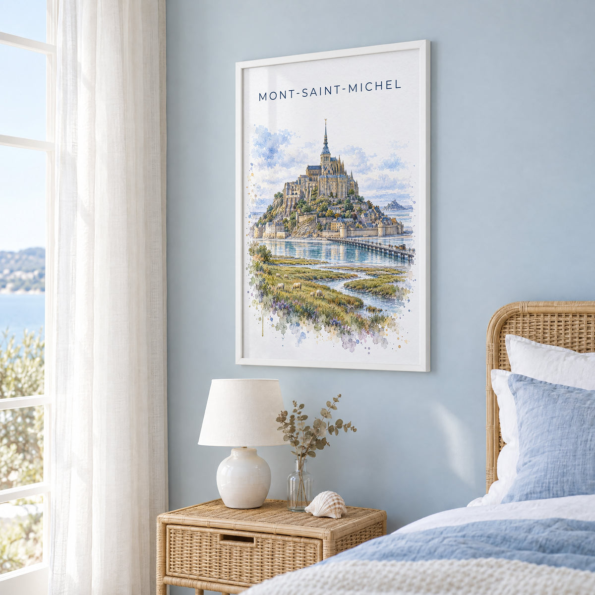 Mont-Saint-Michel watercolor print in a white frame on a pale blue wall beside a rattan bed in a coastal bedroom