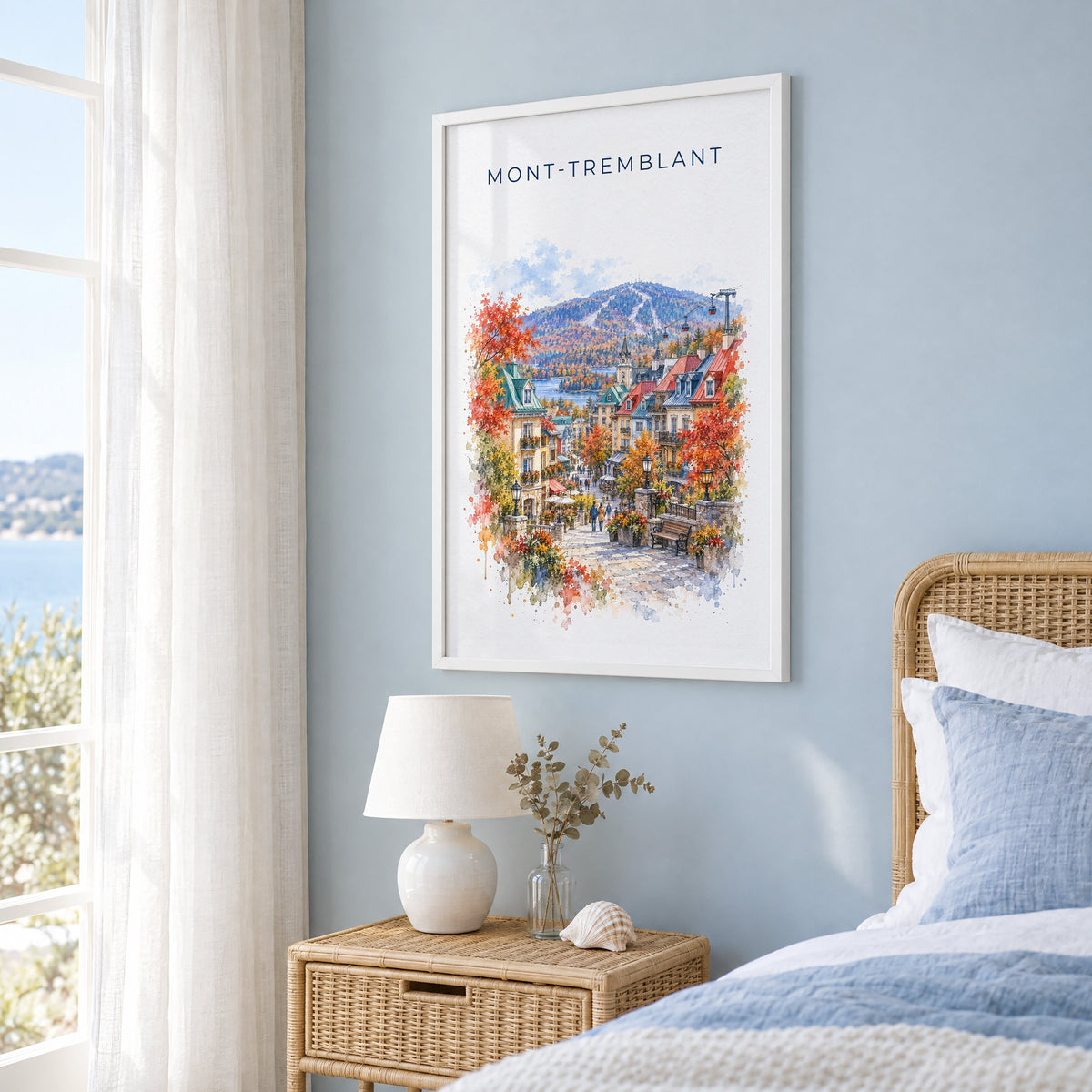 Mont-Tremblant watercolor print in a white frame on a pale blue wall beside a rattan bed in a coastal bedroom