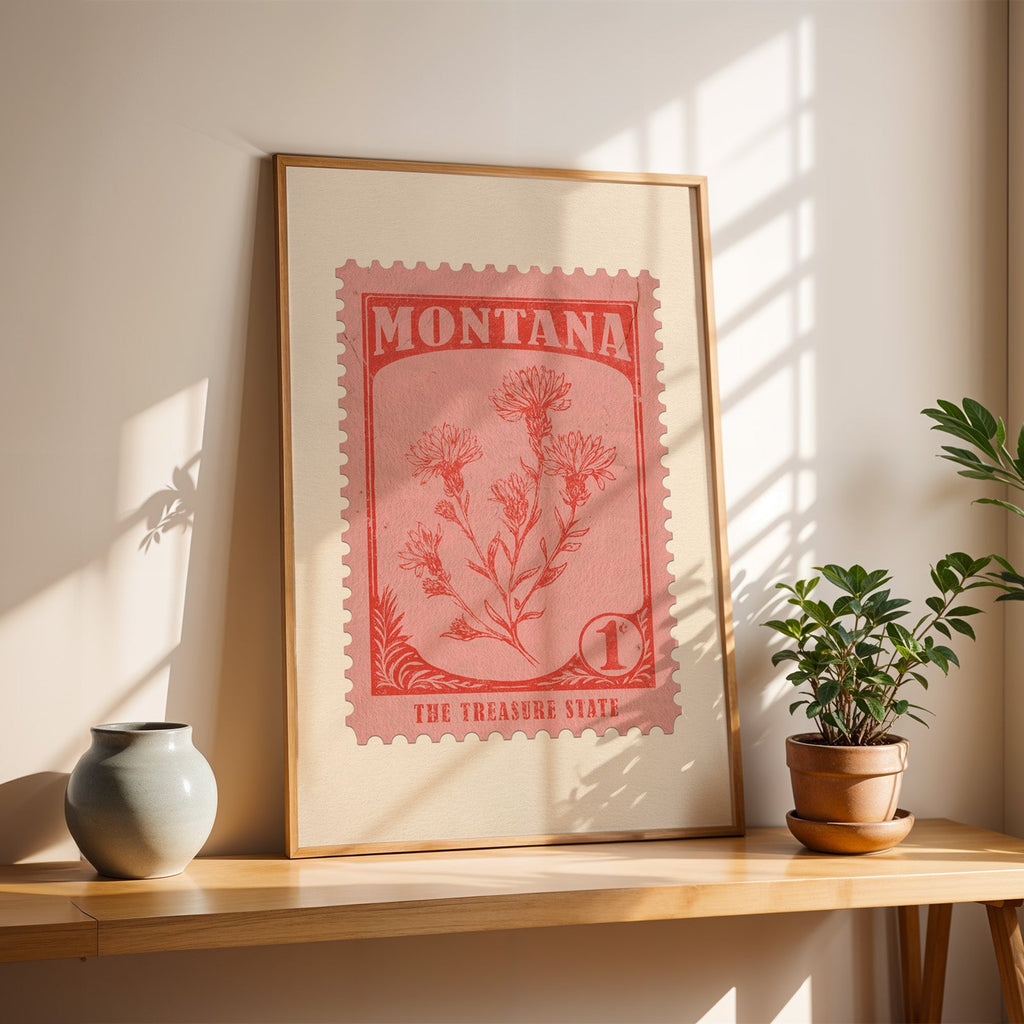 Montana bitterroot stamp print in a light oak frame leaning on a wooden table beside a stoneware vase