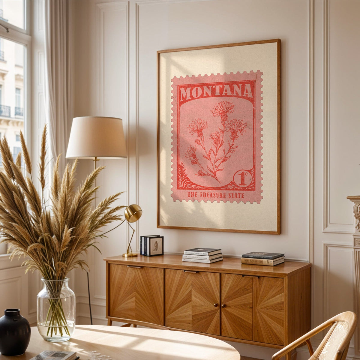 Montana stamp print framed above a wooden sideboard, pampas grass in a glass vase and a floor lamp