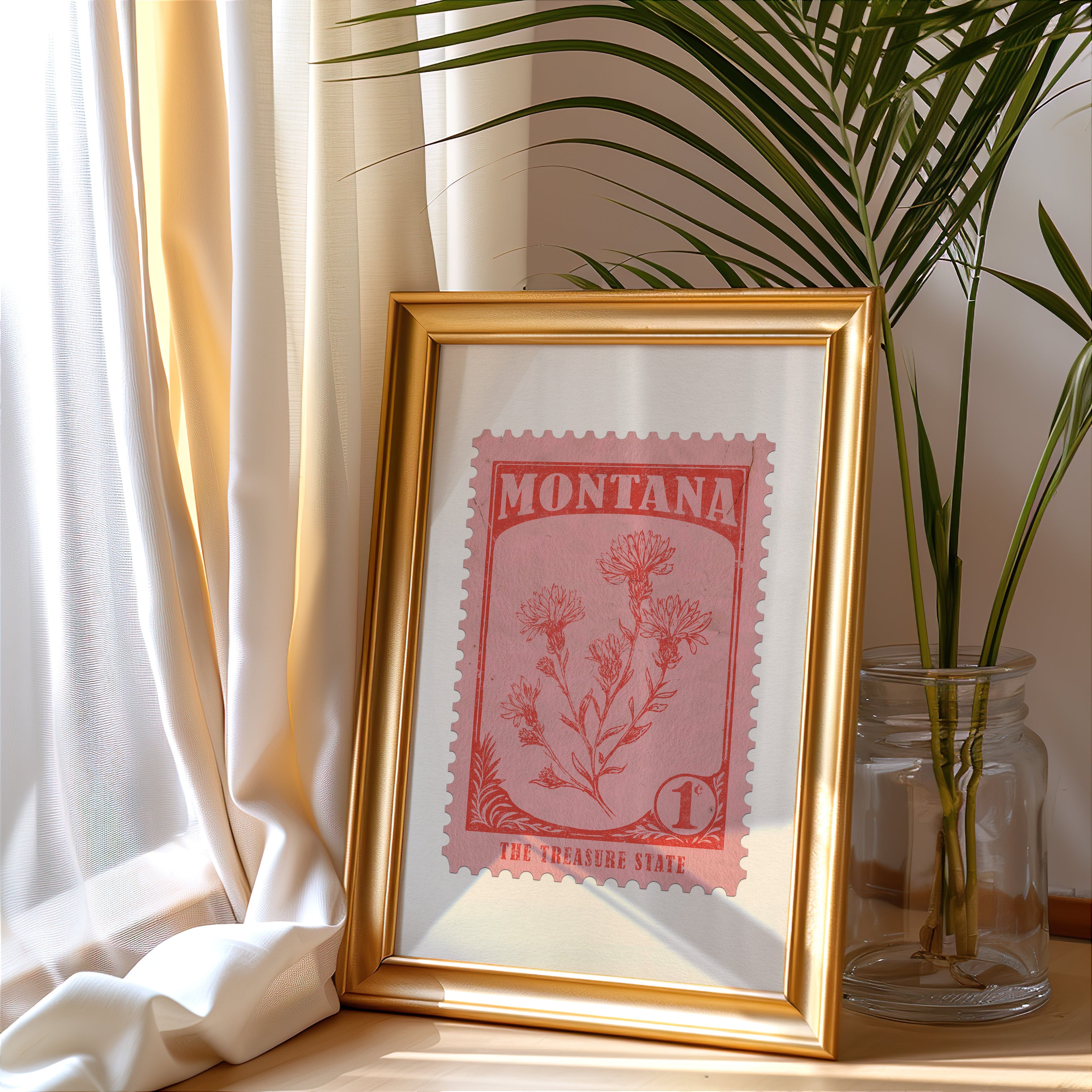 Montana stamp print in a gold frame leaning by a cream curtain with a palm in a glass jar