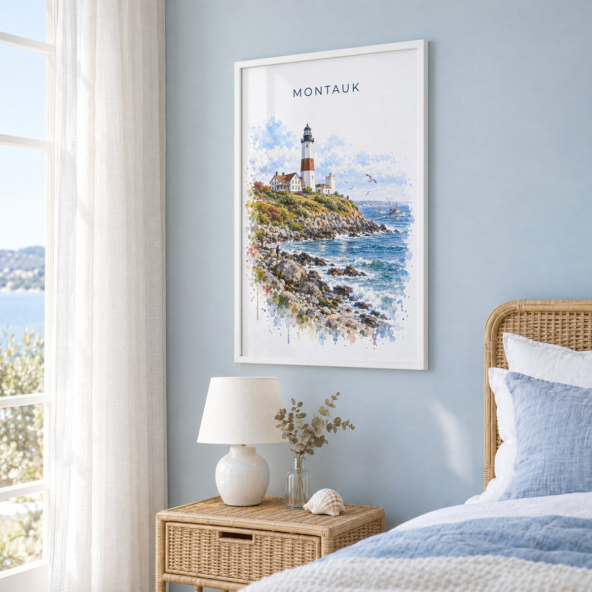 Montauk watercolor print in a white frame on a pale blue wall beside a rattan bed in a coastal bedroom