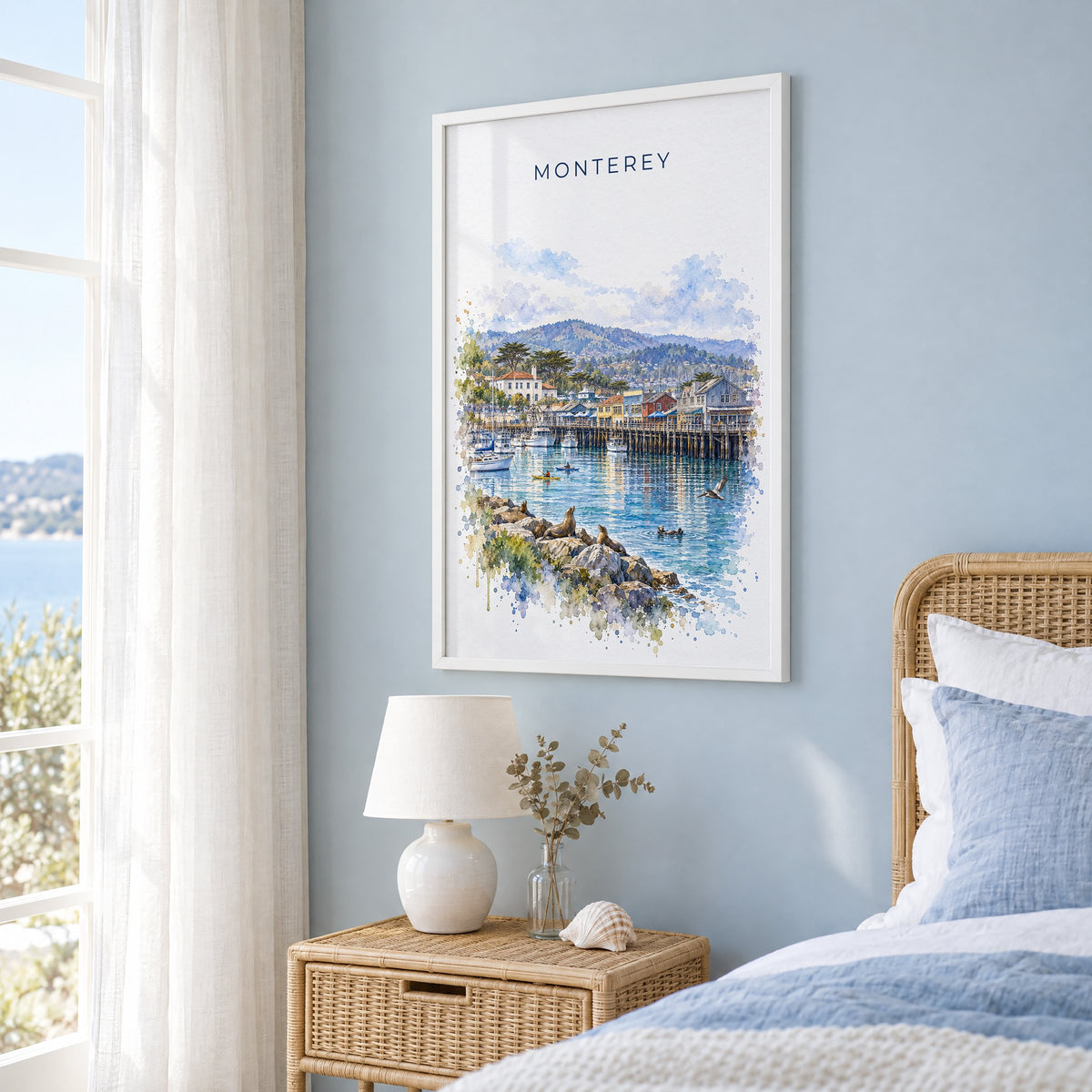 Monterey watercolor print in a white frame on a pale blue wall beside a rattan bed in a coastal bedroom