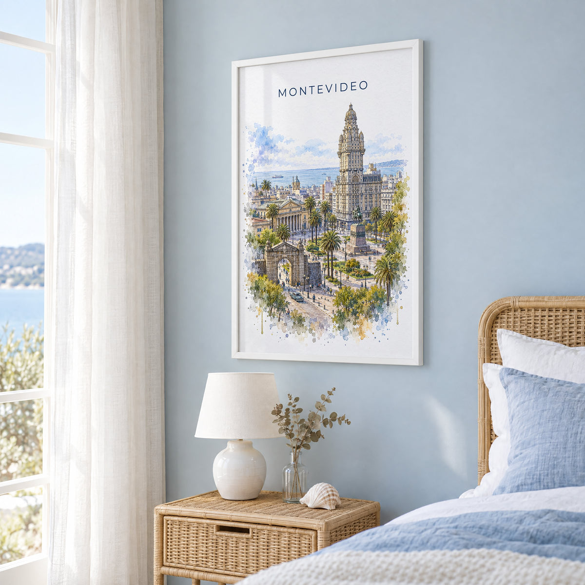 Montevideo watercolor print in a white frame on a pale blue wall beside a rattan bed in a coastal bedroom