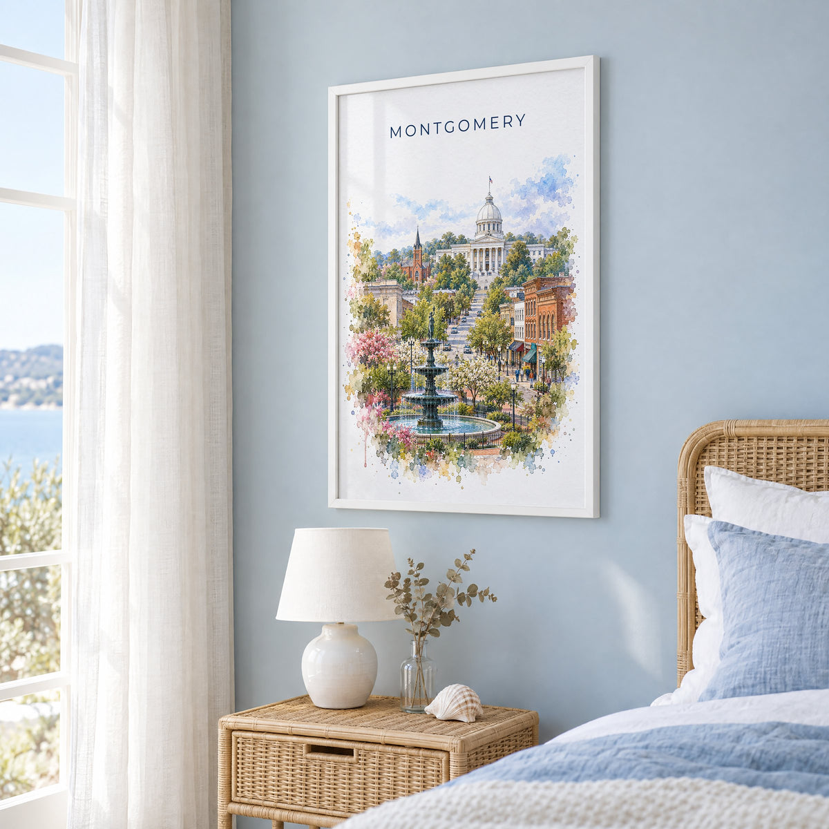 Montgomery, Alabama watercolor print in a white frame on a pale blue wall beside a rattan bed in a coastal bedroom