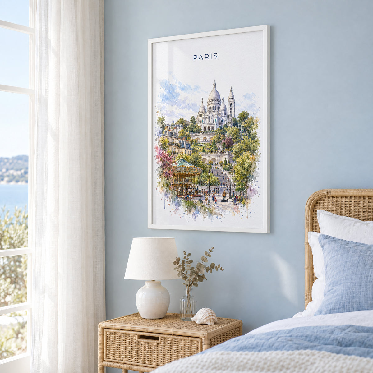 Montmartre Paris watercolor print in a white frame on a pale blue wall beside a rattan bed in a coastal bedroom