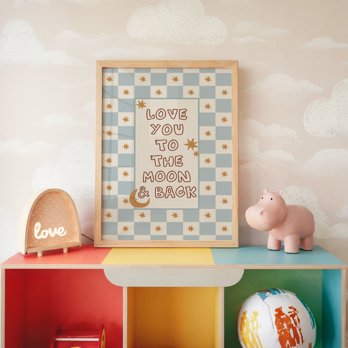 Love you to the moon nursery print in an oak frame on a rainbow toy shelf against cloud wallpaper