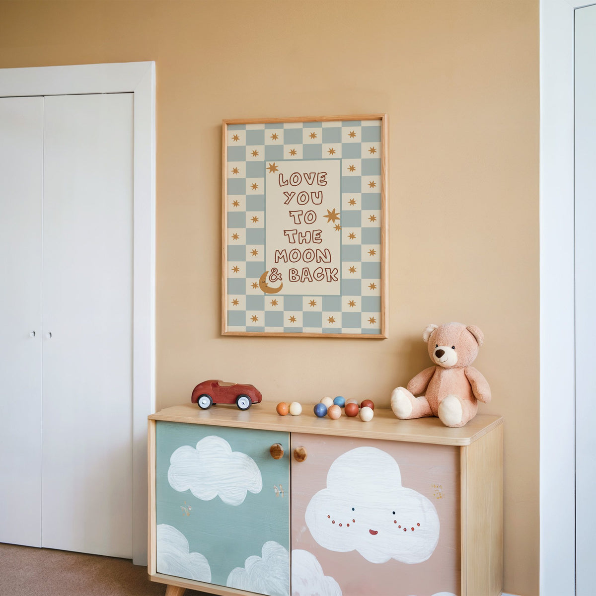Love you to the moon nursery print in an oak frame on a peach wall above a cloud-painted cabinet