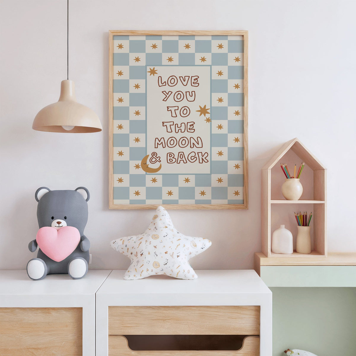 Love you to the moon nursery print in an oak frame above a white dresser with a star pillow and house shelf