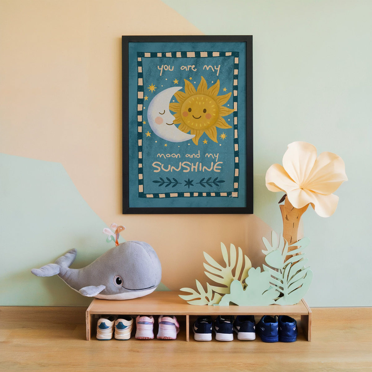 Sleepy moon and smiling sun nursery print in a black frame on a mint and peach wall above a whale plush