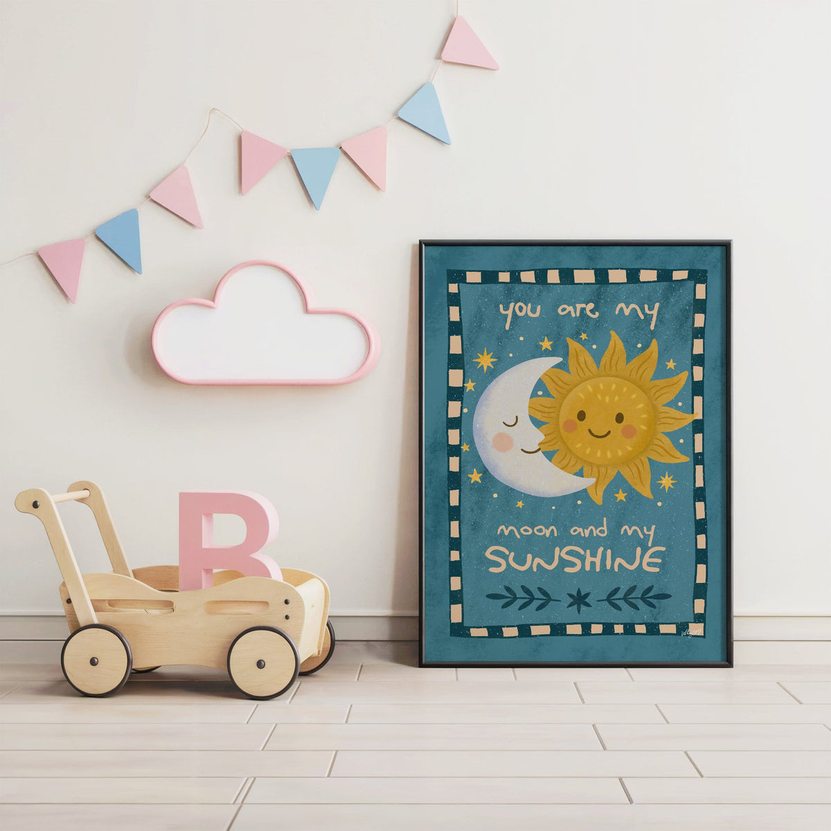 Sleepy moon and smiling sun nursery print in a black frame under pastel bunting by a wooden baby walker