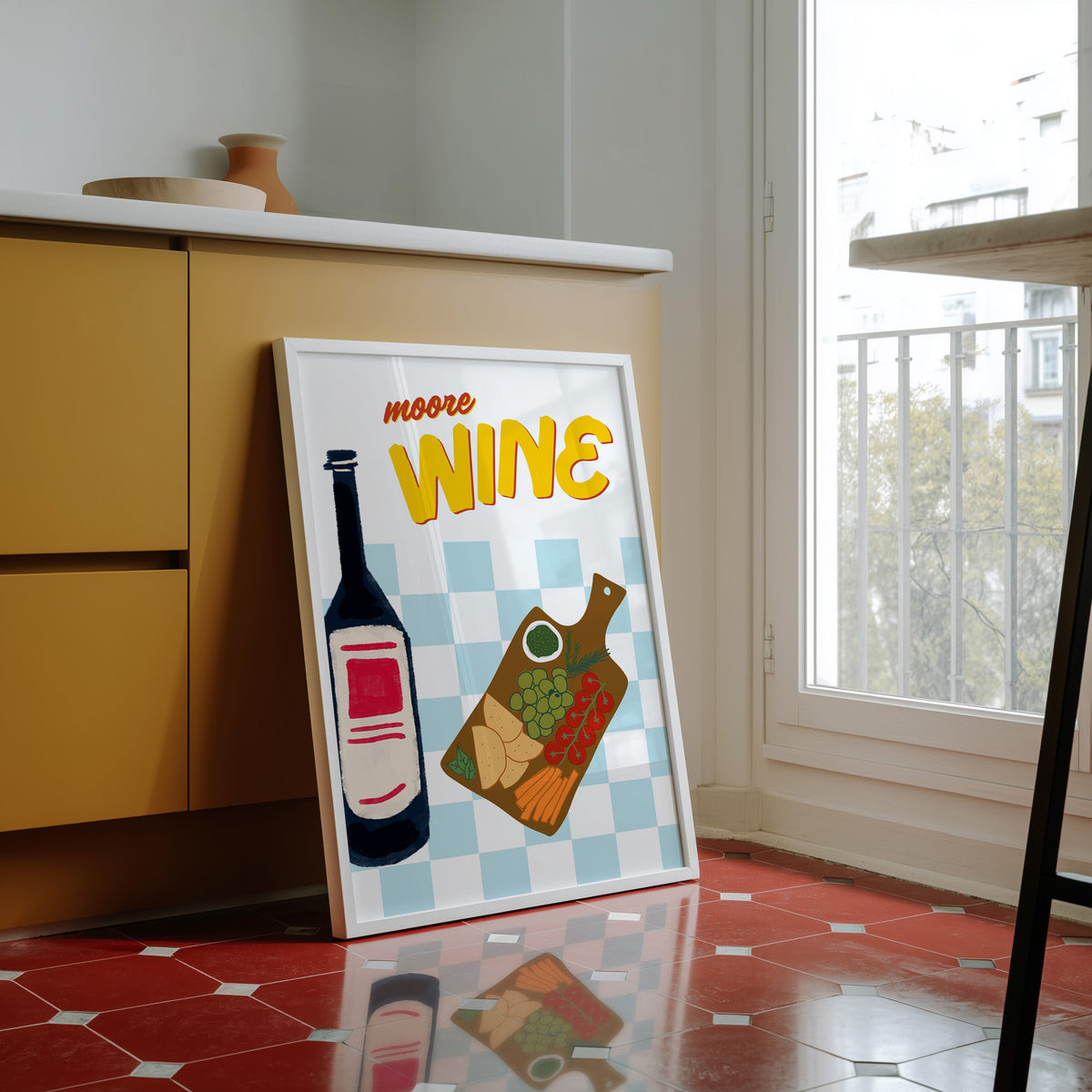 Wine and cheese board print in a white frame against yellow cabinets on a red tiled floor