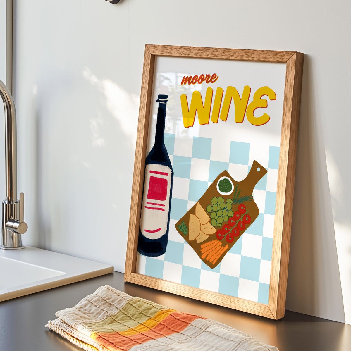 Wine and cheese board print in an oak frame by the kitchen sink beside a striped tea towel