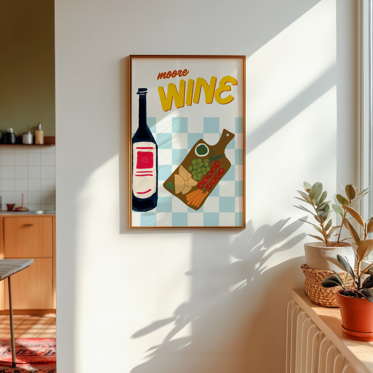 Wine and cheese board print shown in a gold frame in sunlight with plants and a kitchen beyond