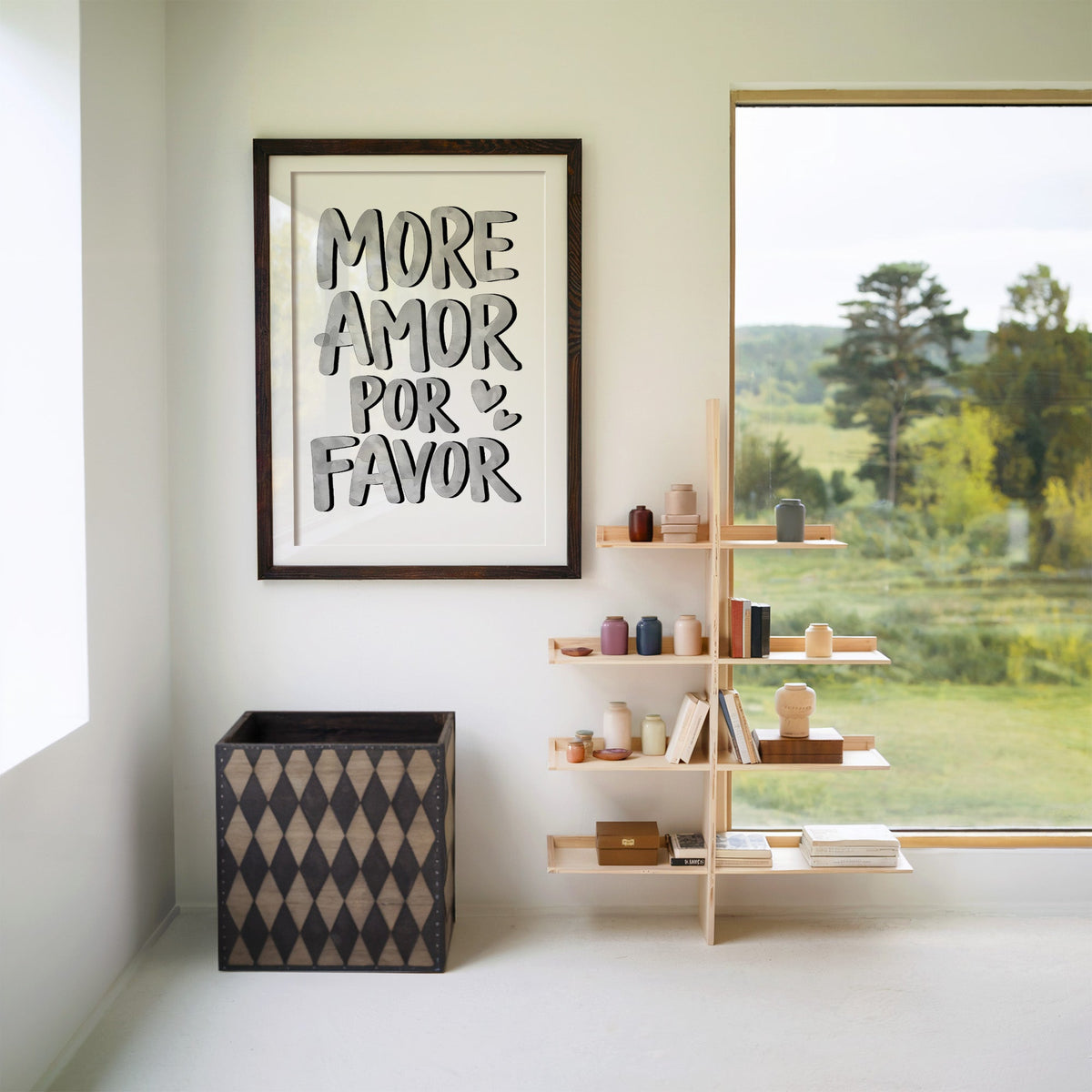 More amor por favor grey lettering print in a walnut frame with a white mat beside wooden shelves and a garden window