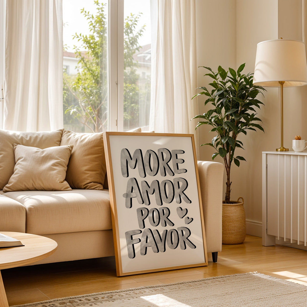 More amor por favor grey lettering print in a light oak frame leaning on a cream sofa beside a floor lamp