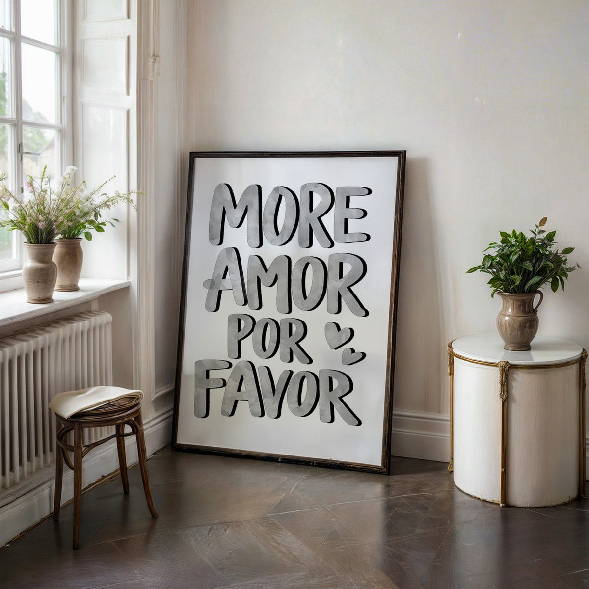 More amor por favor grey lettering print in a black frame on a dark stone floor beside a white side table