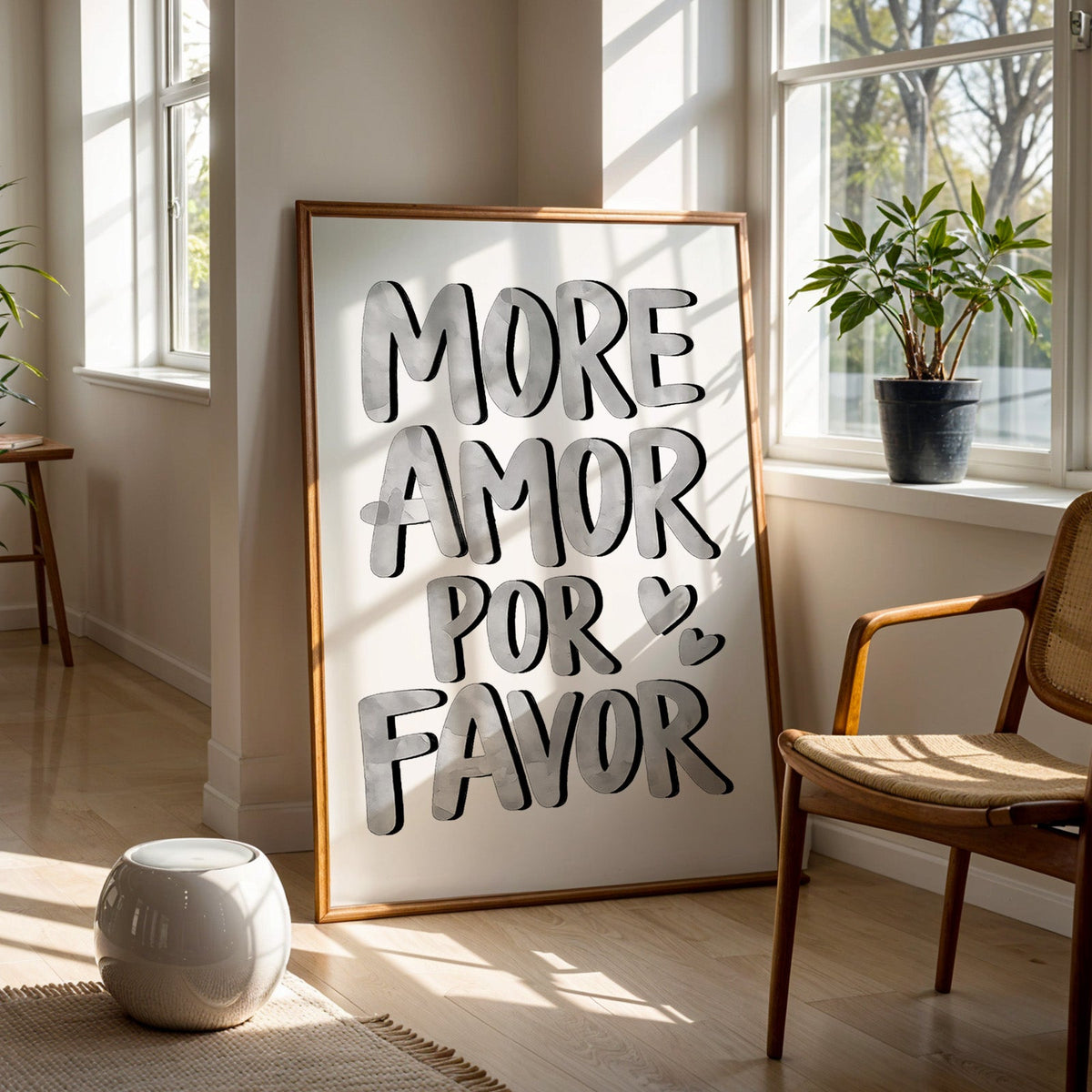 More amor por favor grey lettering print in a walnut frame on a wood floor beside a cane chair and sunny window