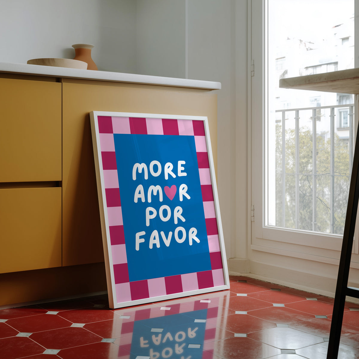 More Amor Por Favor print in a white frame against yellow cabinets on a red tiled floor