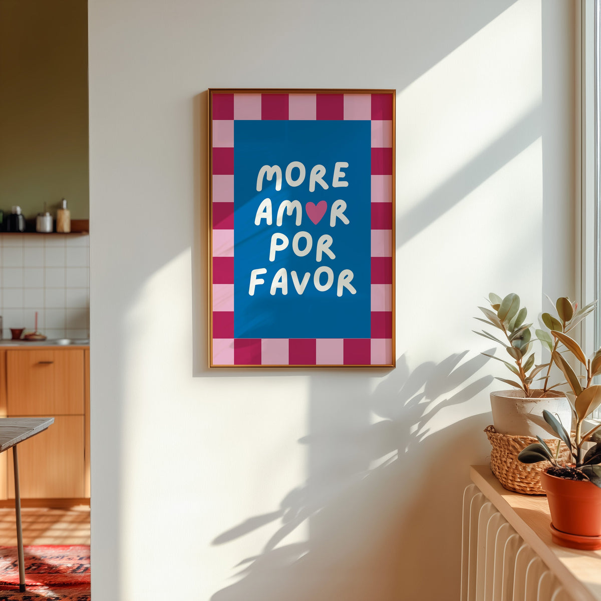 More Amor Por Favor print shown in a gold frame in sunlight with plants and a kitchen beyond